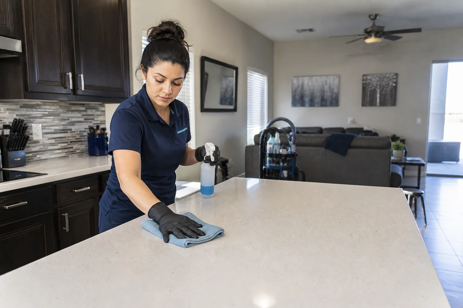 A house cleaner cleaning a kitchen island in a lived-in home